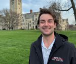 Photo of graduating student Jacob Kahl posing on campus with the iconic Bell Tower behind him.