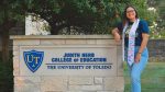 Photo of graduating education student Esparenza Hallauer, who is posing next to the Judith Herb College of Education sign.
